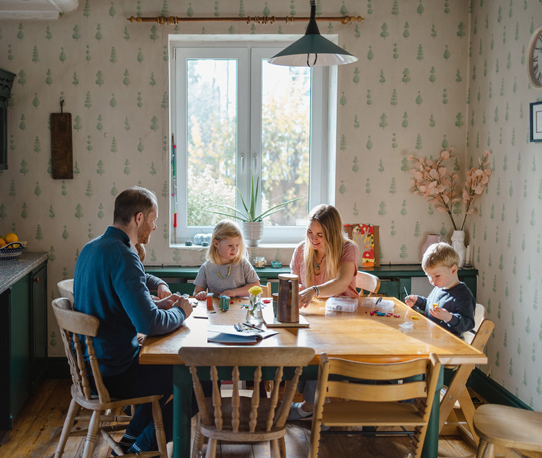 Family gathered at the kitchen table with parents offering encouragement to their young children.