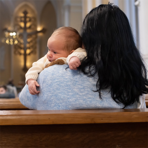 Young mother of an infant sitting in pew alone. Parishes need faith filled communities of young families.